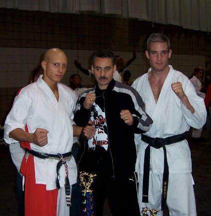 Three martial artists posing together with championship belts