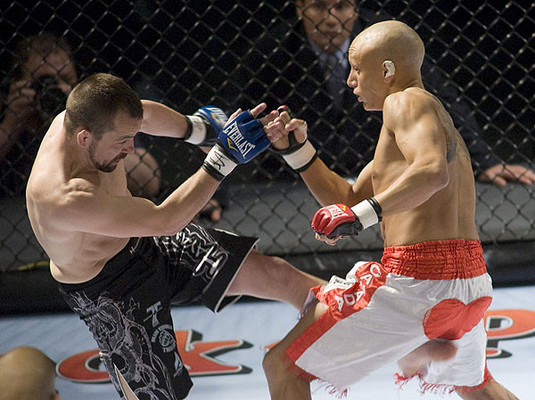 Two mixed martial arts competitors exchanging kicks in a cage